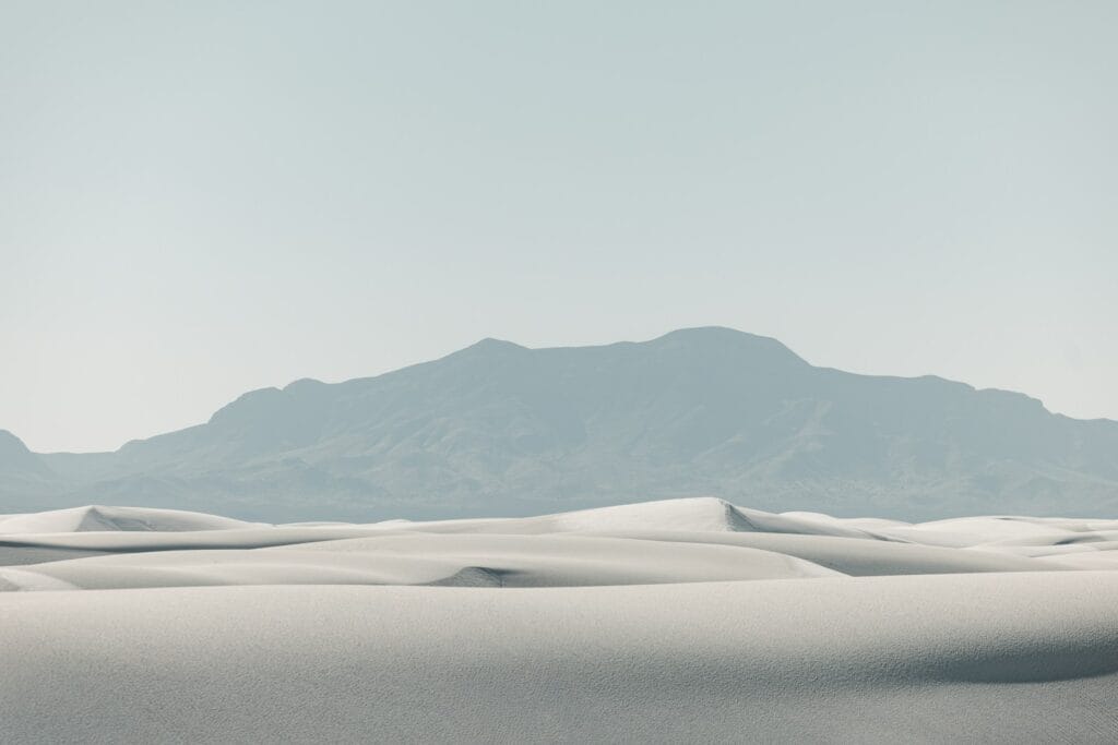Dunas de areia brancas com uma cadeia montanhosa distante.